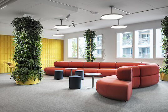 Loungebereich mit rotem Sofa, Pflanzenwänden und runden Pendelleuchten der Serie Basic Neo.