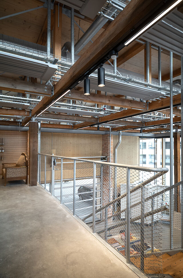 Innenansicht eines Treppenbereichs im Håndværkskollegiet mit sichtbaren Holzträgern, Metallkonstruktionen und zwei schwarzen Midpoint-Strahlern von Lightnet an der Decke