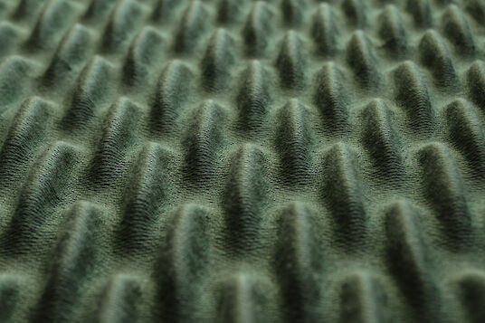 Close-up of a dark green acoustic material with a regular, three-dimensional wave structure.