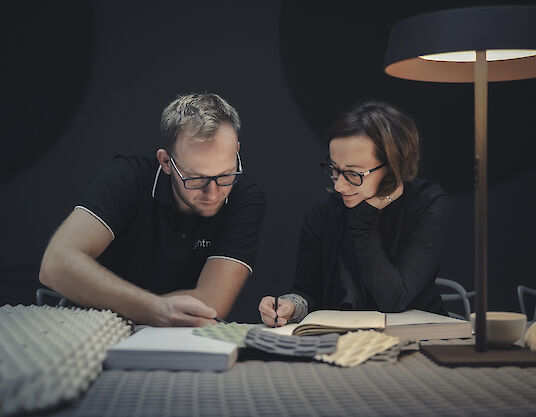 Two designers examine fabric samples for the Serenity luminaire under a Beam Me Up table luminaire.